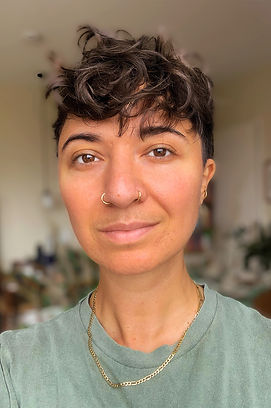 Porträt von queer Illustrator*in EL BOUM mit kurzen braunen Haaren und goldener Halskette, der*die in die Kamera lächelt