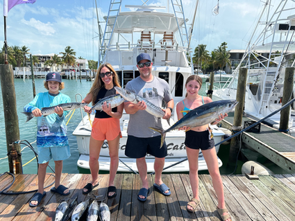 amily photo with fresh‑caught fish beside the Catchin’ Caicos 60' Hatteras yacht—Turks and Caicos fishing charter.