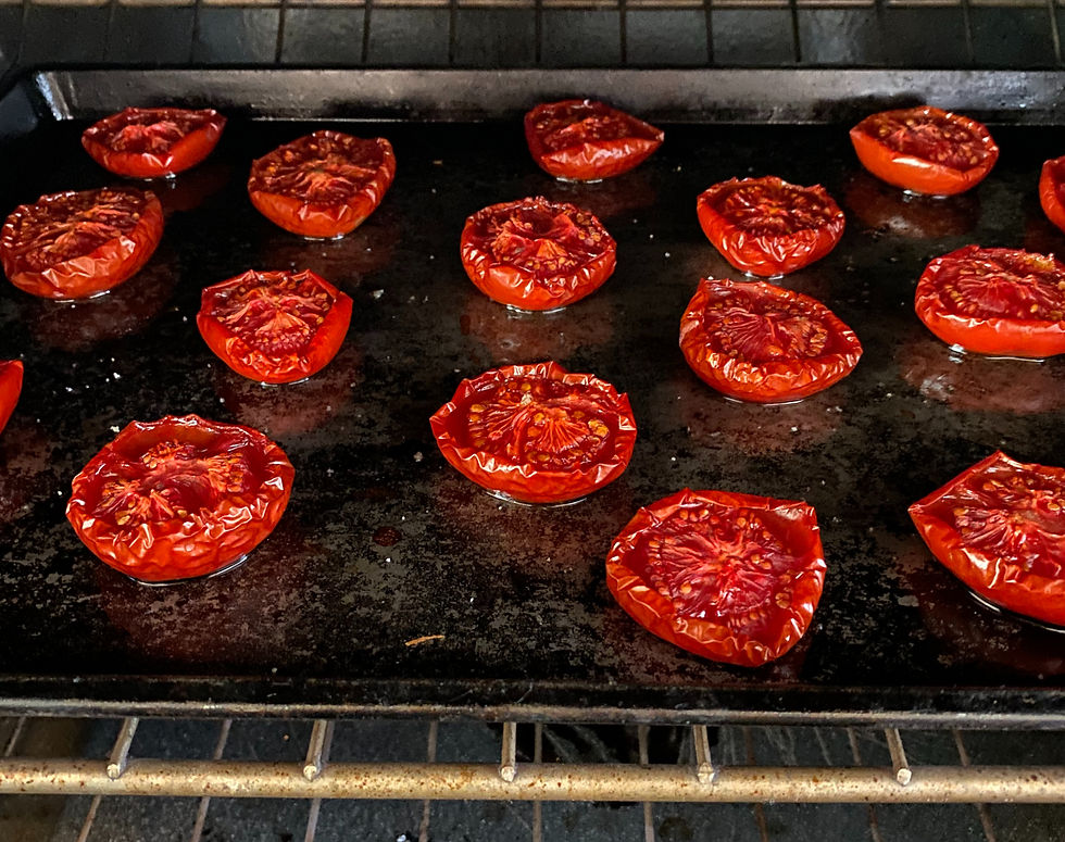 Halved tomatoes on a sheet pan in the oven, lightly dried and wrinkled on the edges
