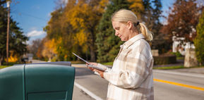 Blond woman in a ponytail collecting her mail from the mailbox on a sunny autumn day