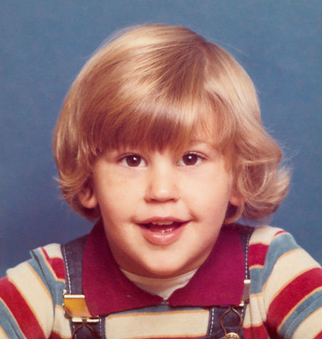 A portrait photograph of a young boy has been damaged during removal from a frame or mount. Sections have been torn off the print surface and the edge of the frame has left a pronounced line around the subject.