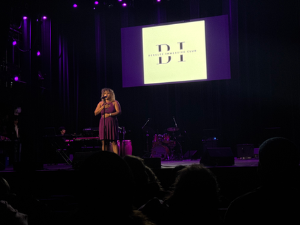 a woman singing in front of a screen that says Berklee Immersive Club