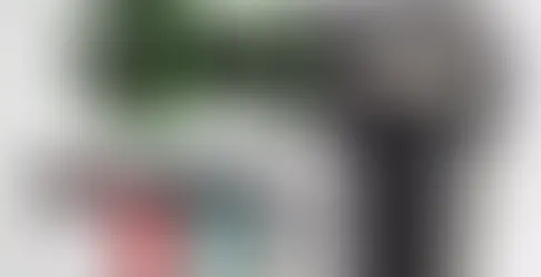 istola de massagem preta com bolas vibratórias verdes, várias cores ao fundo e acessórios de cabeça sobre base branca.