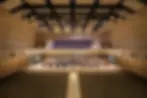 Wide shot of a modern wood panelled auditorium featuring a student orchestra on the stage and a choir on the second level