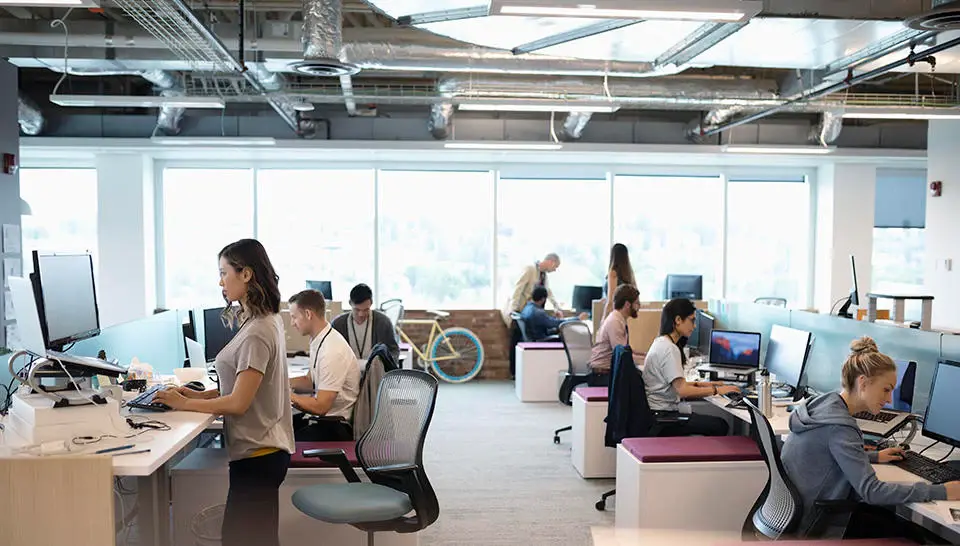 Open office floorplan with various employees sitting and/or standing at their desk working away