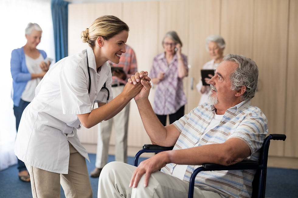 Doctor holding the hand of a senior patient in a wheelchair, while senior residents chat in the background