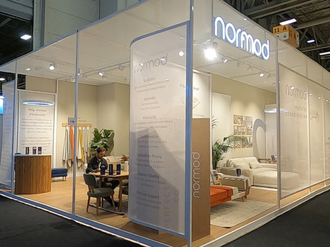 Normod standı fuar alanında, beyaz zemin ahşap detaylar ve tasarım ürünleri sergileniyor.