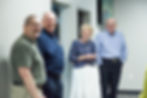 Four senior adults in a church hallway smiling while in a conversation with one another.
