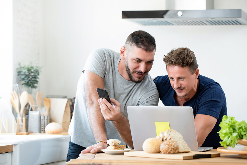 Two men work on a laptop in their kitchen