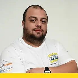 Professional headshot of George G wearing a white Balkan Dispatch branded shirt with crossed arms