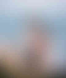 Son riding on dad's shoulder while dad holds mom's belly by the beach shore