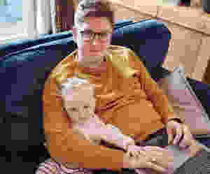 A man sits with his young son on a couch while working on his laptop