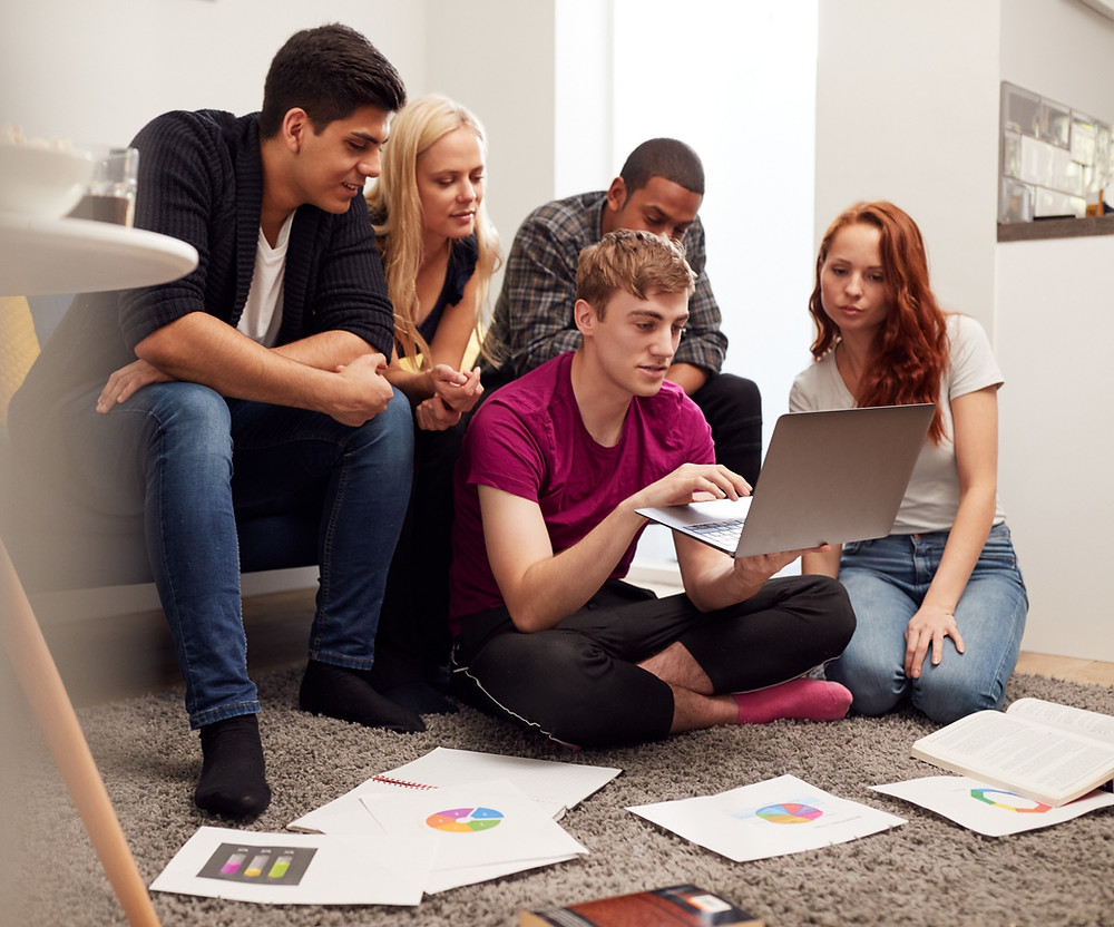 A group of school students revising for their secondary school exams, looking at laptop with revision paper on floor