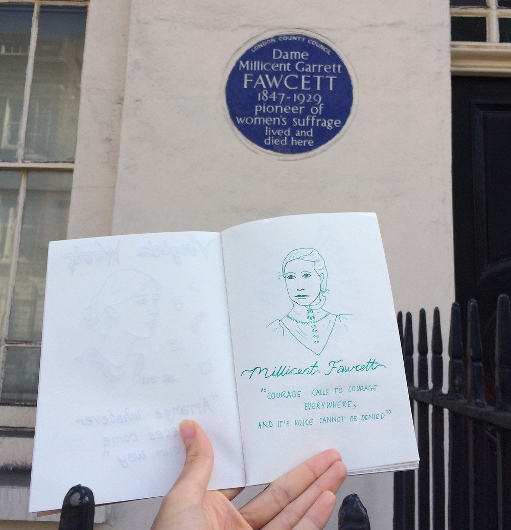 Nina holding up a sketch of Dame Millicent Garrett Fawett next to her blue plaque in London.