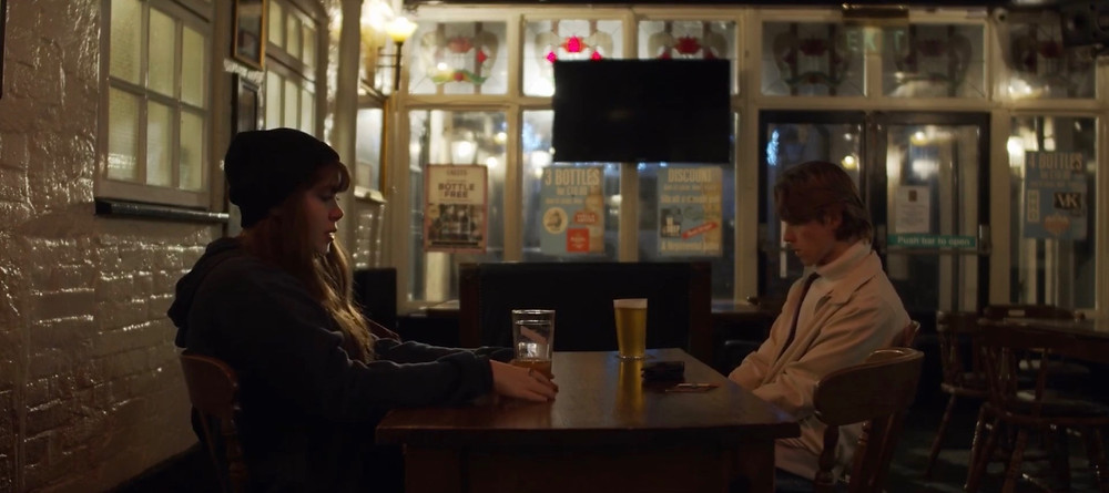 This image shows the two main characters of the short film, Annie (left) and Kyle (right) as they sit at a brown table in a dimly light bar, drinking beer.