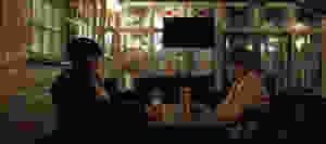 This image shows the two main characters of the short film, Annie (left) and Kyle (right) as they sit at a brown table in a dimly light bar, drinking beer.
