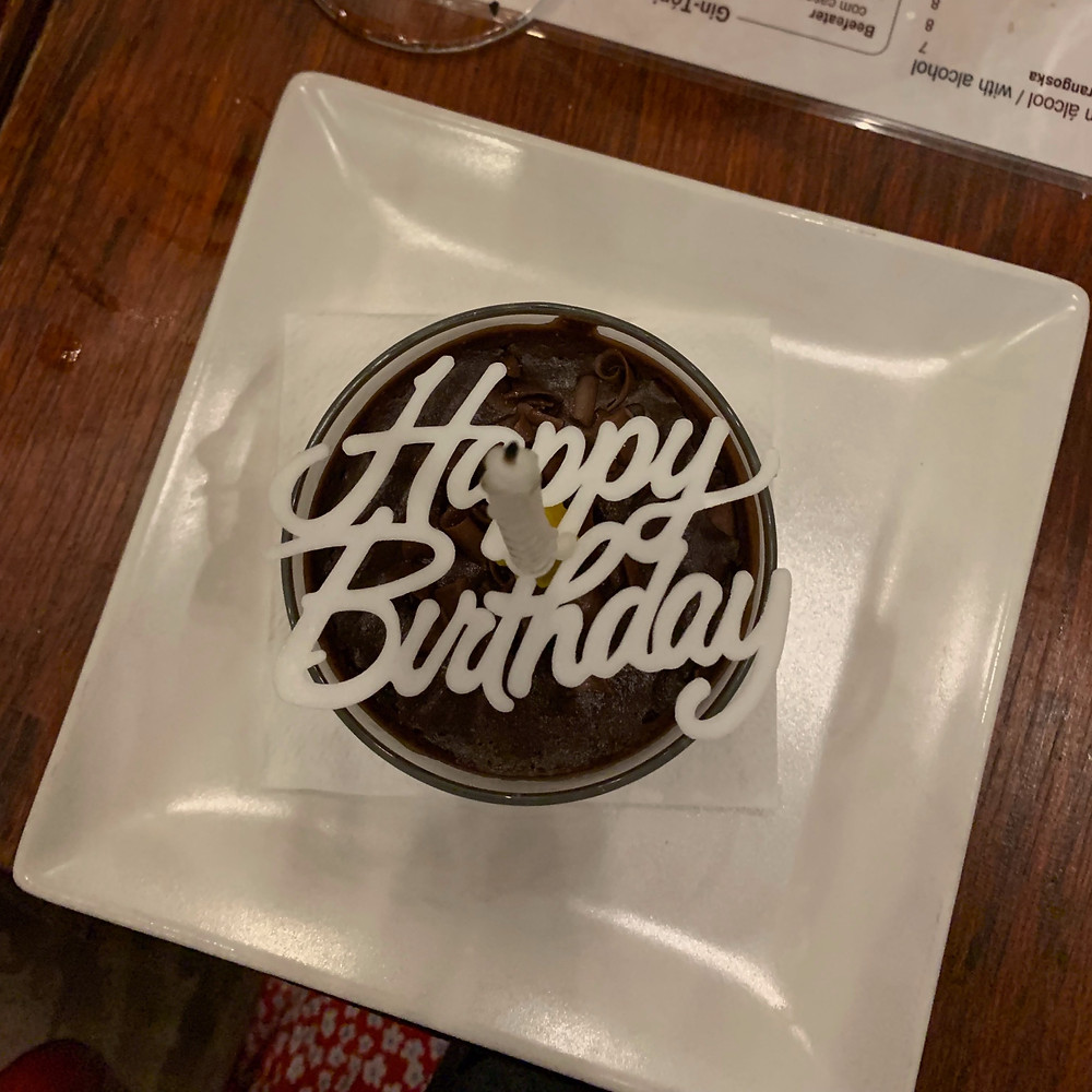 A white candle over a cursive "Happy Birthday" stencil over a chocolate mousse