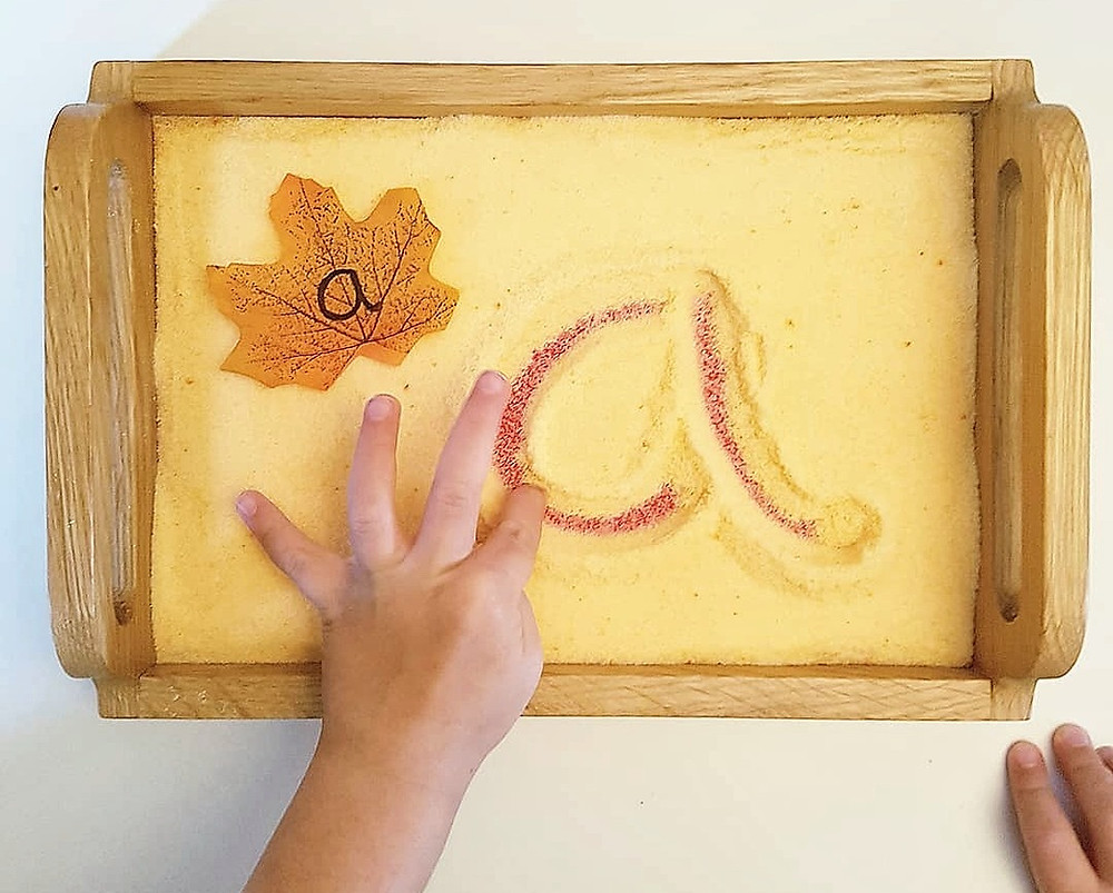 child writing letter a in yellow salt