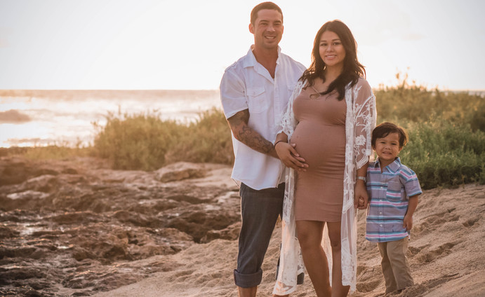 Dad holding mom's belly while son holds mom's hand