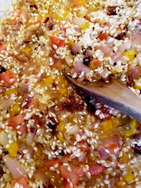 Close-up of paella cooking with rice, onions, and tomatoes