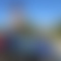 A group of cyclists pose in front of blue road sign with the text “Bicycle Friendly Community” with mountains and forested landscape in the background.  