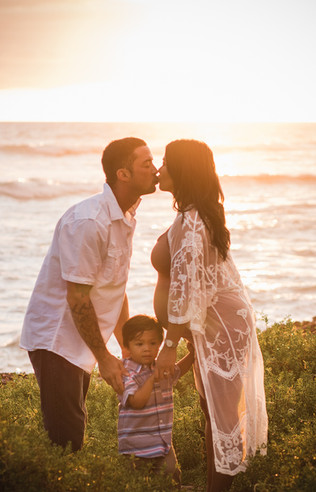 Mom and dad share a kiss with son in-between them looking at camera