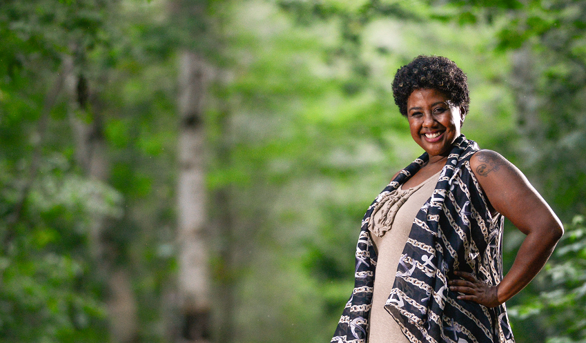 proud black woman standing in wooded forest, with a big smile.