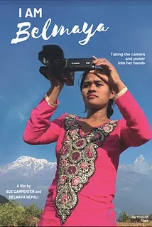 A young Nepali woman in a pink dress looks through the viewfinder of a video camera with the Himalayas in the background.