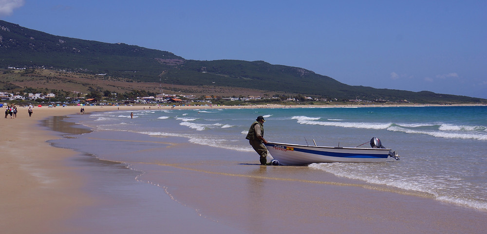 Long, quiet, sandy beach at Bolonia with fisherman and boat.