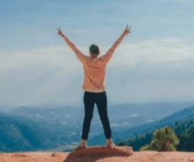A woman is seen from behind with her arms raised in triumph is standing on a mountain top.