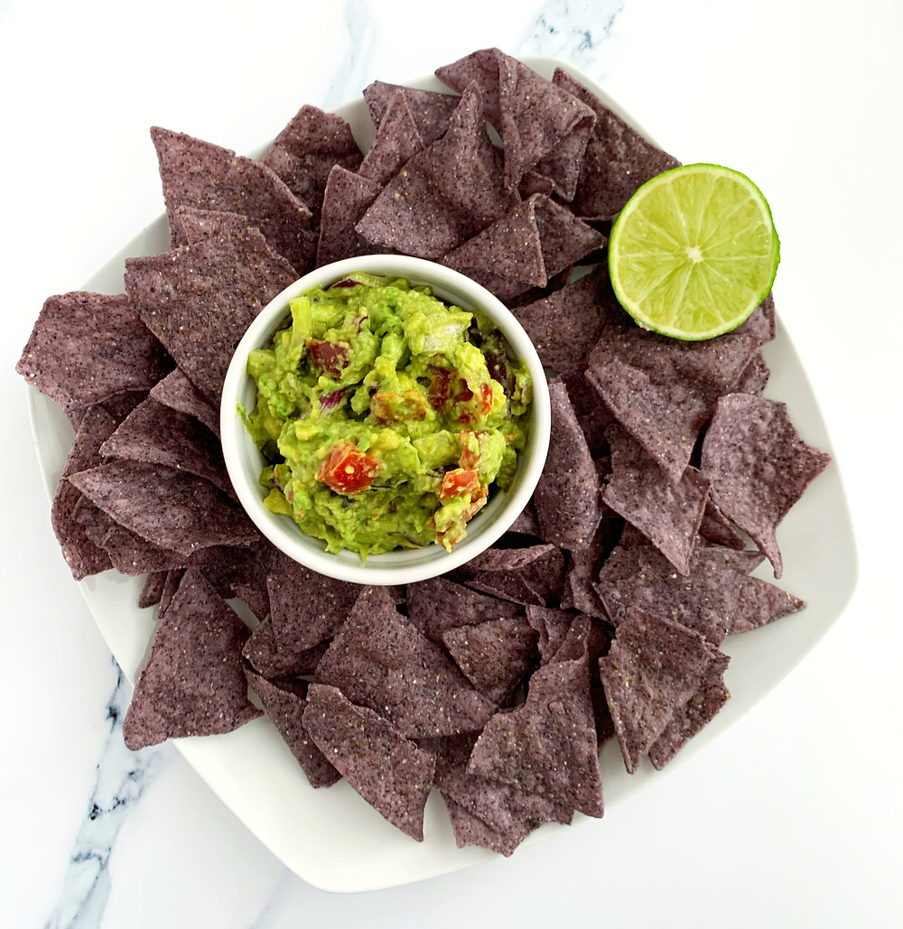 overhead shot of creamy 5-minute guacamole with blue tortilla chips and a slice of lime