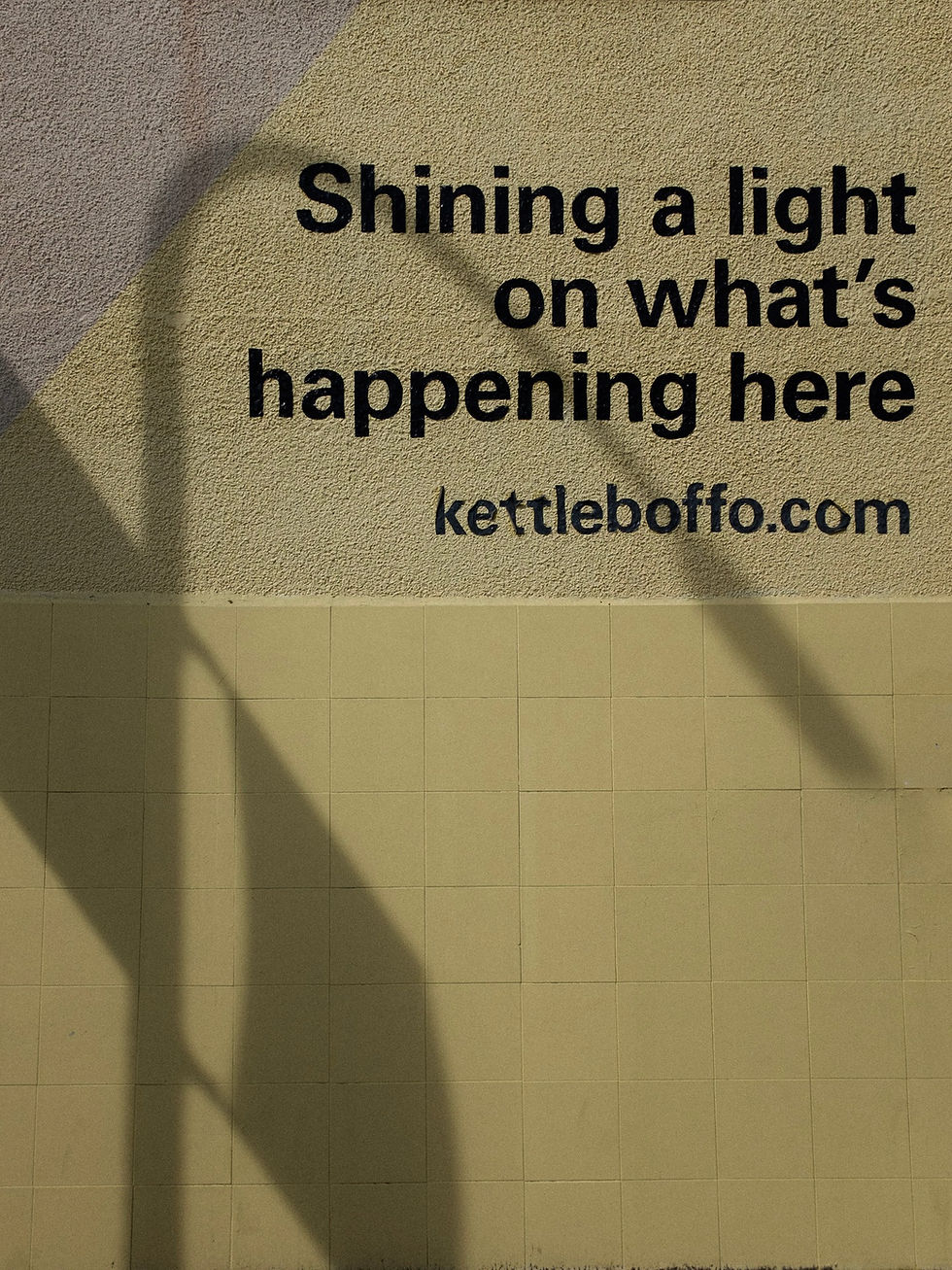 A shadow of a lamp post is projected onto a wall: the text reads, "Shining a light on what;s happening here..."