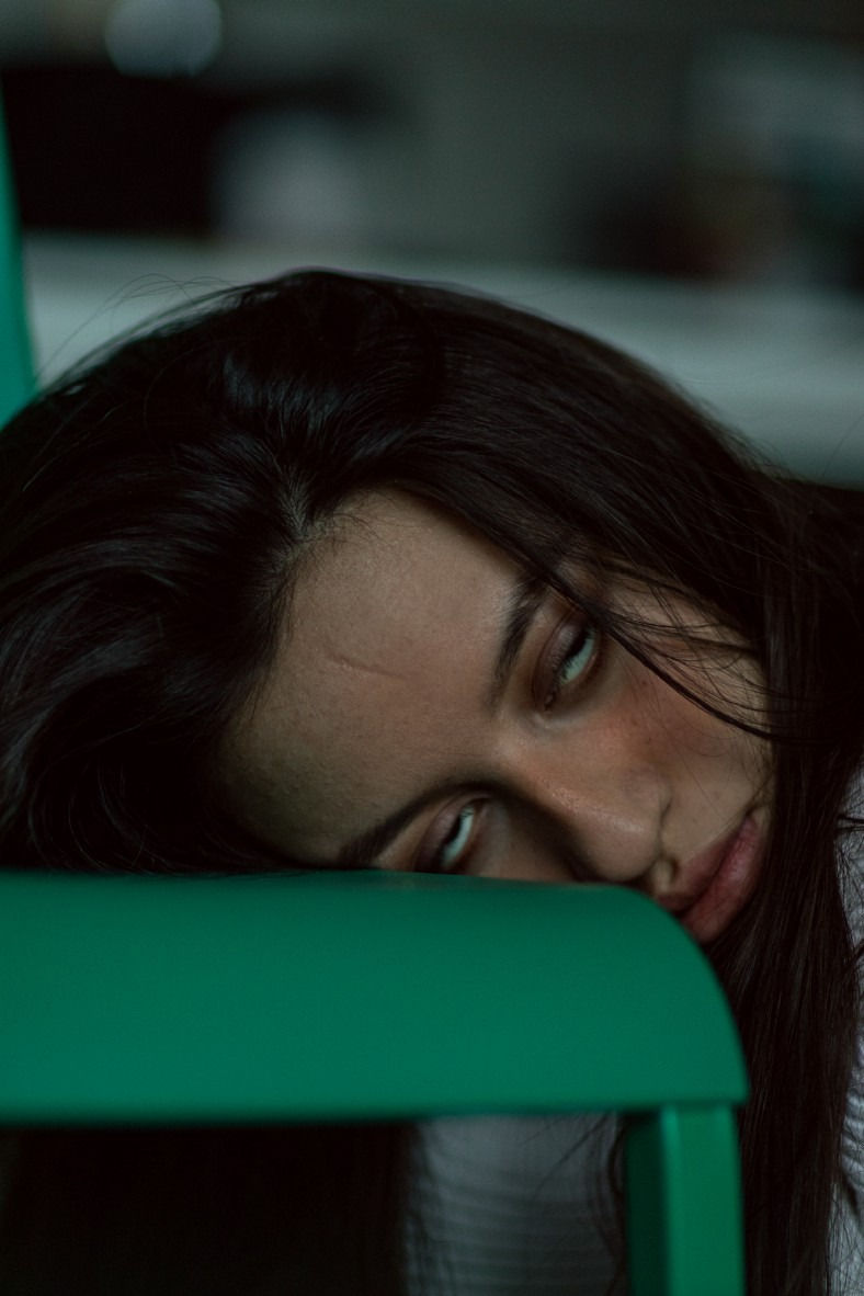 Madwoman, eyes rolling, head on green chair