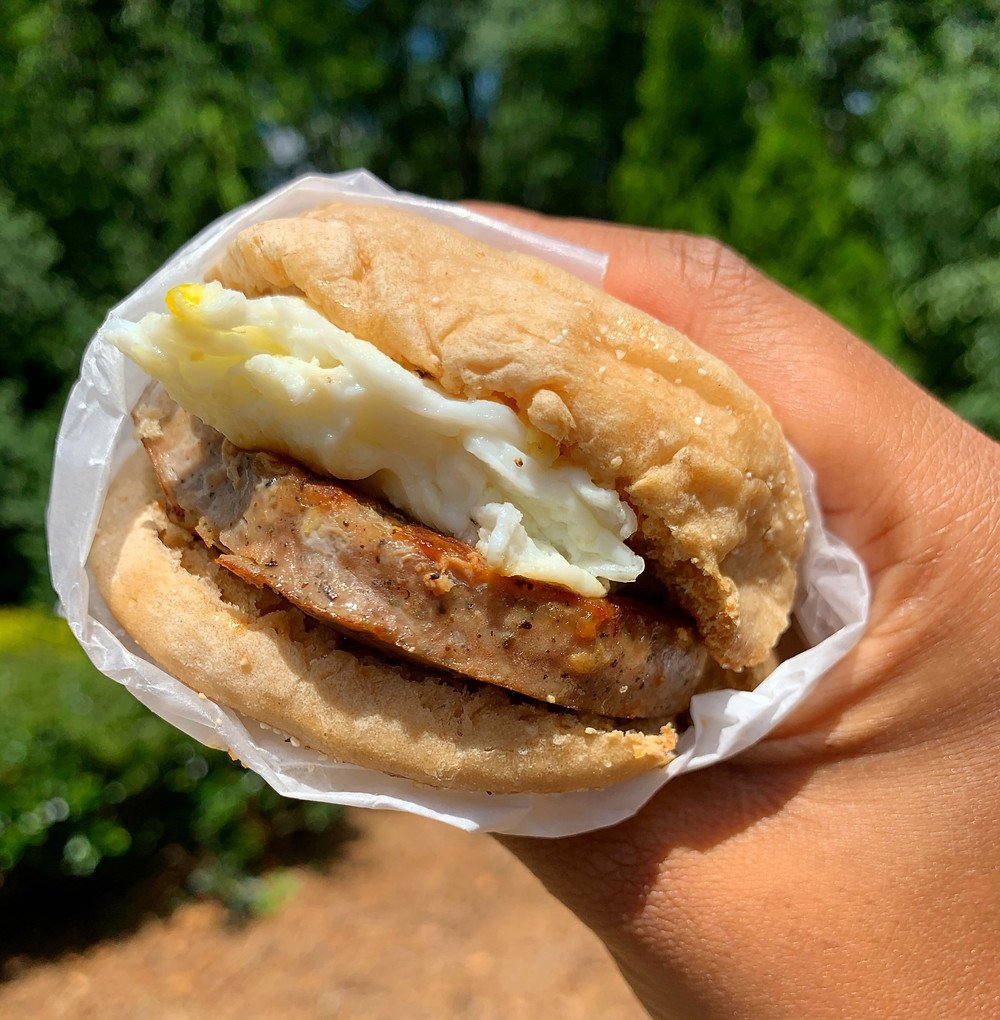 hand is holding a sausage, egg, and cheese breakfast sandwich on an english muffin