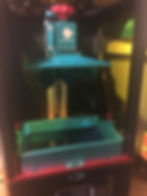 Inside of 3D printer showing build area. There is a flat metal build plate at the top with printed dice hanging off the bottom. Below this is a vat containing liquid resin