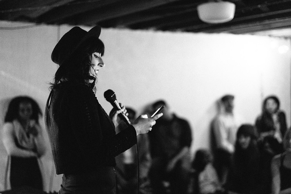 Performer reading poetry on stage with audience in the background