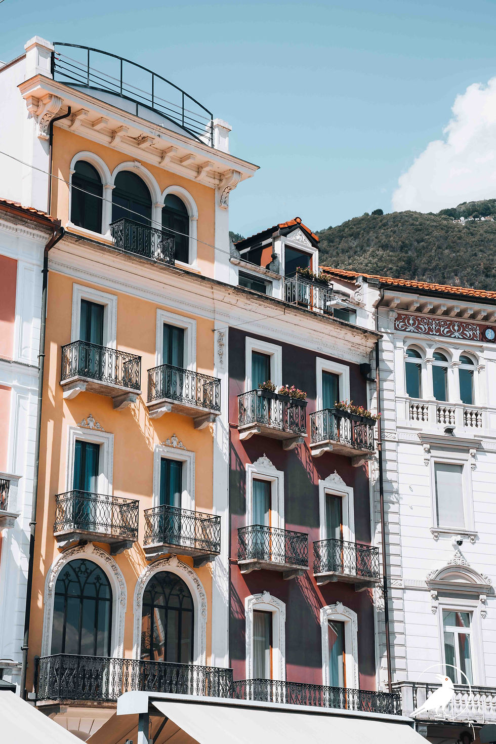 Colorful Mediterranean apartment façades with wrought-iron balconies under a blue sky, mountains behind