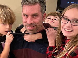 A father holding his three young children, capturing a moment of everyday family life and the quiet courage of patience and presence.
