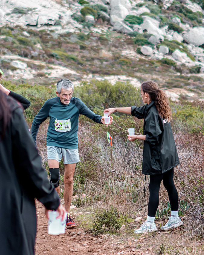 Coureur avec dossard 232 recevant boisson sur sentier rocheux.