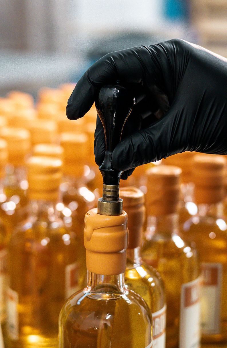 Main gantée de noir scellant une bouteille d'huile ambrée sur chaîne de production.