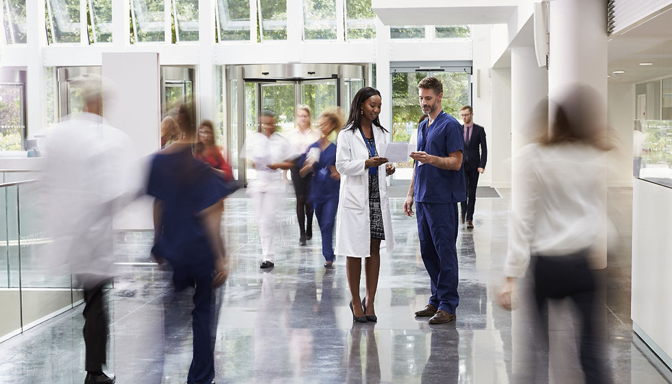 Doctors in a hall with other medical professionals walking by (blurred out)