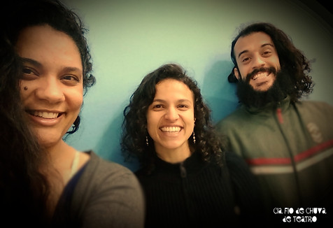 Retângulo de borda vermelha com três pessoas sorrindo, na esquerda uma mulher parda de cabelos longos escuros, no meio uma mulher parda de cabelo preto e blusa preta e na direita um homem branco de cabelo preto combrido, barba grande e blusa verde.