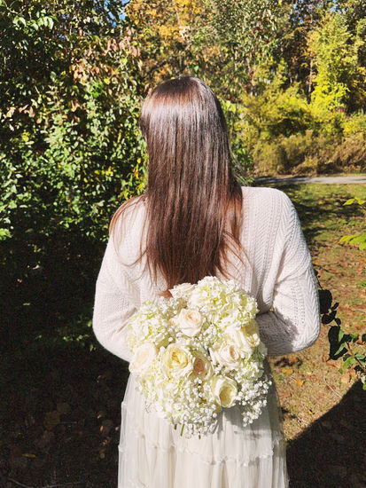 a woman in a white sweater is holding a bouquet of white flowers