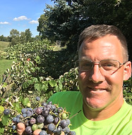 Main with glasses holding grapes and smiling.