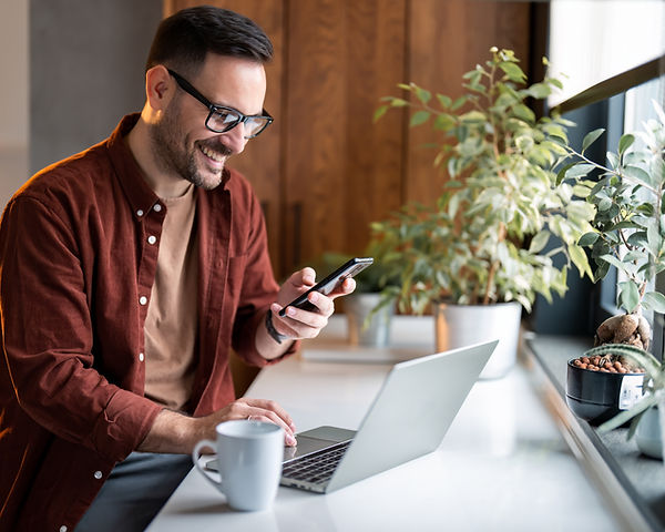 Satisfied modern millennial man in stylish casual clothes using smartphone and laptop comp