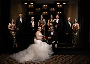 Bride and groom with full wedding party in formal attire posing indoors, luxury wedding group portrait.