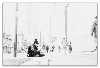 High-contrast black and white portrait of a homeless man staring directly at the camera, his figure rendered in deep black against overexposed white tones.