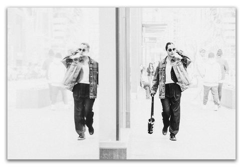 High-contrast black and white street photograph of a woman walking in downtown Toronto, with both her figure and her reflection in a storefront window rendered as deep black silhouettes against overexposed white surroundings.