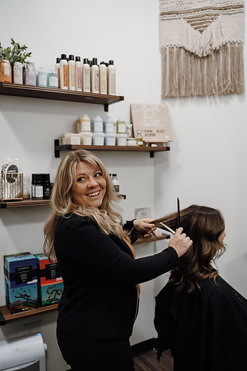 Jessica smiling looking behind her while she combs a clients hair.