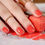 Thumbnail: Manicured nails showing of a vibrant coral orange nail color, resting atop a set of matching nail polish wraps